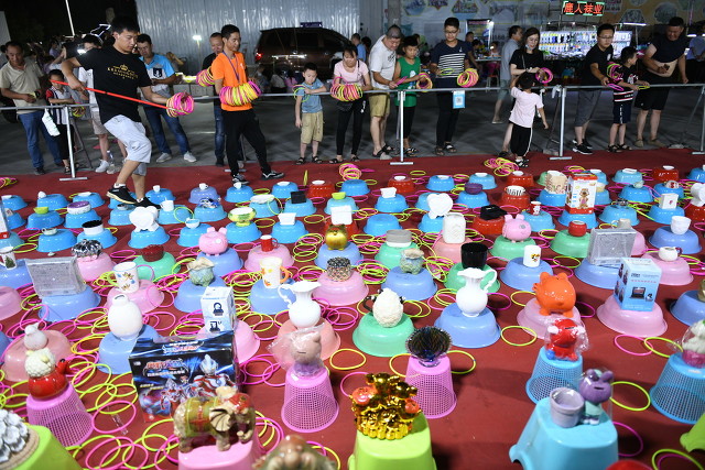 套圈的摊位旁挤满了大人和孩子,套圈奖品丰富,有杯子,碗,存钱罐,玩具
